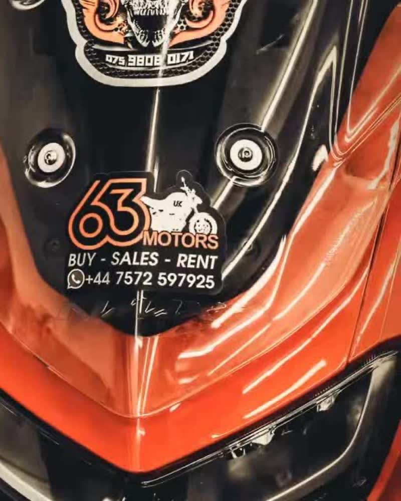 Close-up of a customer's orange motorbike with a 63 Motors sticker and contact number on the headlight cowl