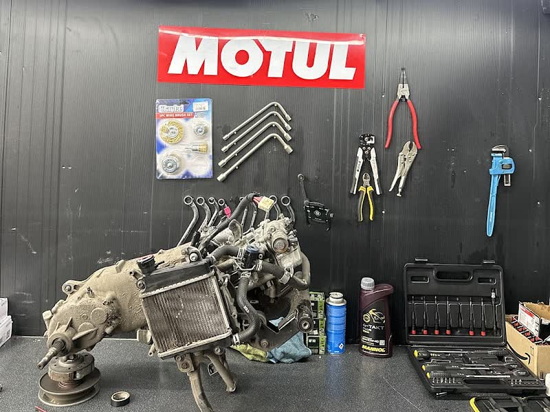A stripped motorcycle engine on the workbench at 63 Motors, tyres and tools on the wall behind
